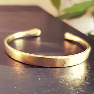 Pode incluir: Um bracelete simples de metal dourado. O bracelete é liso e tem uma forma ligeiramente arredondada.