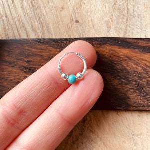 May include: A silver hoop earring with a turquoise bead in the center. The earring is small and delicate.