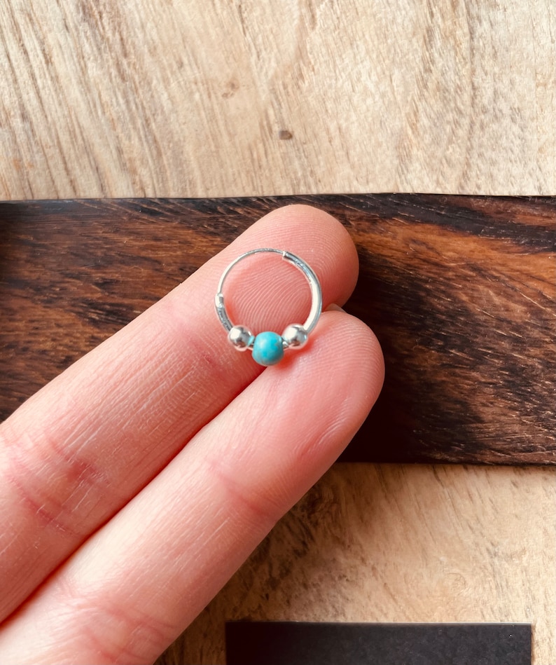 May include: A silver hoop earring with a turquoise bead in the center. The earring is small and delicate.