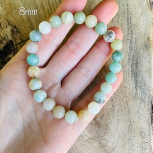 May include: A green and white beaded bracelet with 8mm beads. The bracelet is made of natural stones and is shown on a hand.