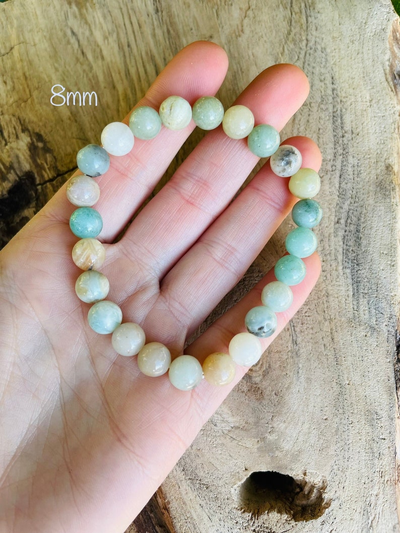 May include: A green and white beaded bracelet with 8mm beads. The bracelet is made of natural stones and is shown on a hand.
