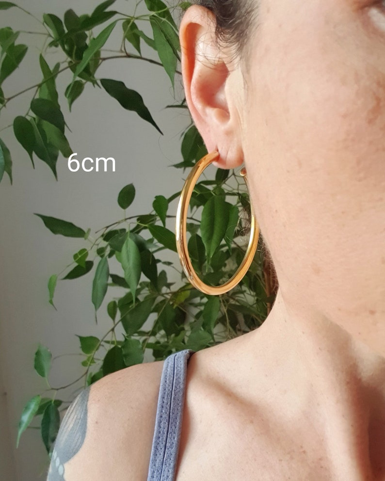May include: Gold hoop earrings with a diameter of 6 cm. The earrings are shown on a person's ear.