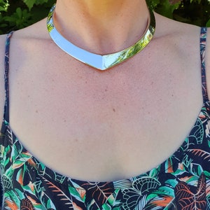 May include: A silver choker necklace with a V-shaped design. The necklace is worn by a person with a floral print top.