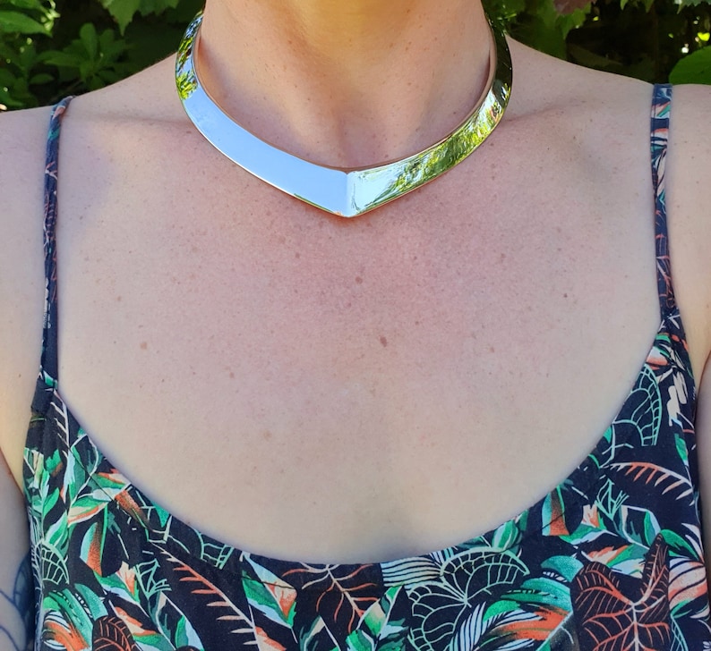 May include: A silver choker necklace with a V-shaped design. The necklace is worn by a person with a floral print top.