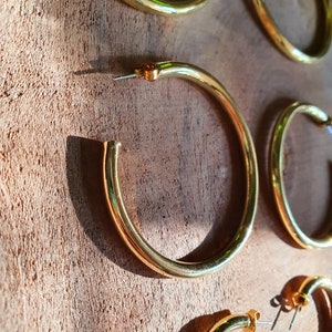May include: Four gold hoop earrings of different sizes on a wooden surface.