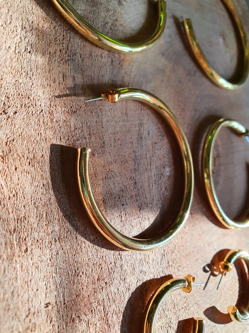 May include: Four gold hoop earrings of different sizes on a wooden surface.