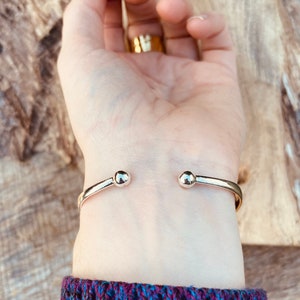 May include: A silver bangle bracelet with rounded ends. The bracelet is on a person's wrist.