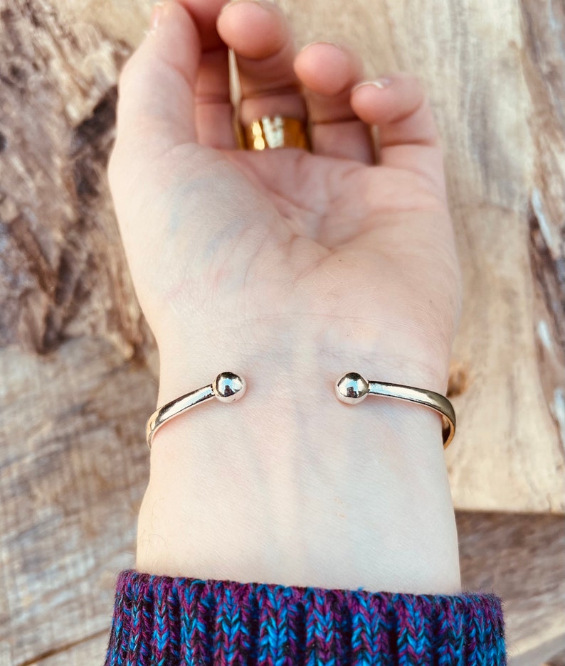 May include: A silver bangle bracelet with rounded ends. The bracelet is on a person's wrist.