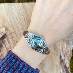 May include: A silver bracelet with a geometric design. The bracelet is made of metal and has a diamond-shaped center piece.