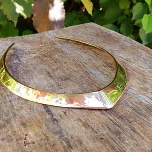 May include: A gold-toned metal choker necklace with a wide, flat, and slightly pointed design. The necklace is made of a hammered metal, giving it a textured surface.
