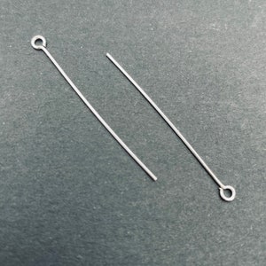 Peut inclure: Deux épingles à tête argentées avec une boucle à une extrémité. Les épingles à tête sont sur une surface grise.