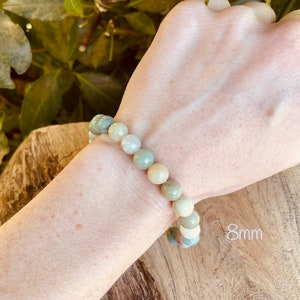May include: A bracelet made of light green, white, and beige round beads. The beads are approximately 8mm in diameter. The bracelet is worn on a person's wrist.