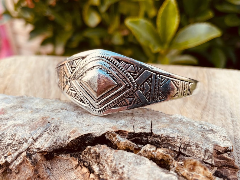 May include: A silver bracelet with a geometric design. The bracelet is made of metal and has a diamond-shaped center piece.
