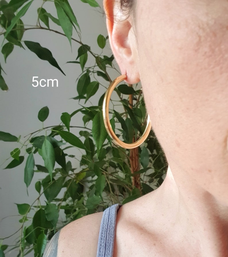 May include: Gold hoop earrings with a diameter of 5 cm. The earrings are shown on a person's ear.