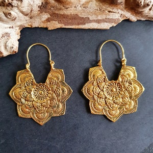 May include: A pair of gold-toned hoop earrings with a detailed mandala design. The earrings are made of metal and have a circular shape with a floral pattern.