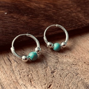 May include: A pair of silver hoop earrings with turquoise beads. The earrings are small and delicate.