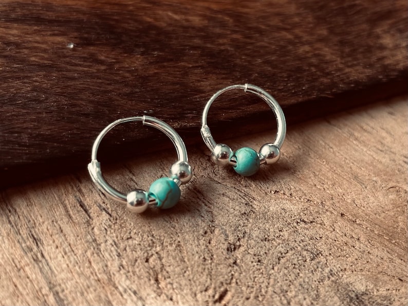 May include: A pair of silver hoop earrings with turquoise beads. The earrings are small and delicate.