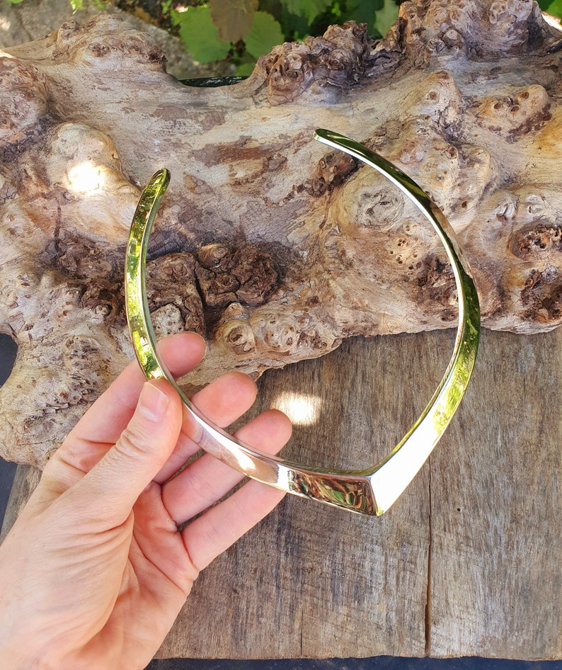 May include: A silver metal choker necklace with a V-shaped design.