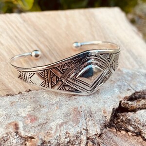 May include: A silver bracelet with a geometric design. The bracelet is made of metal and has a shiny finish.