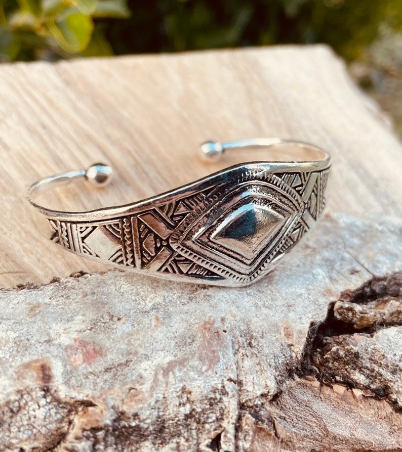 May include: A silver bracelet with a geometric design. The bracelet is made of metal and has a shiny finish.