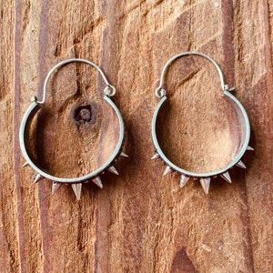 May include: A pair of silver hoop earrings with a row of spikes around the edge.