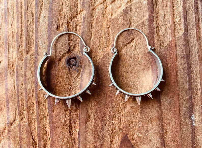 May include: A pair of silver hoop earrings with a row of spikes around the edge.
