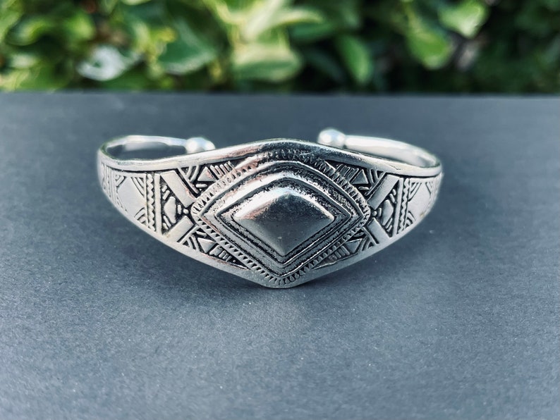 May include: A silver bracelet with a geometric design. The bracelet is made of metal and has a diamond-shaped center piece.