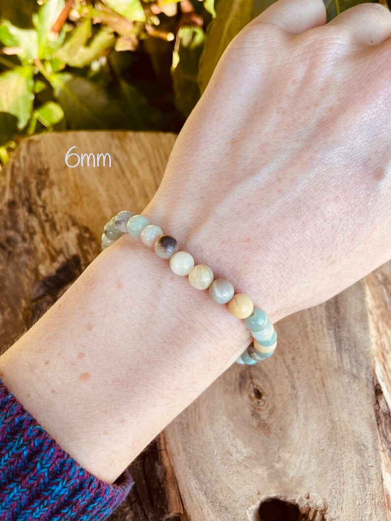 May include: A bracelet made of green, brown, and white 6mm round beads. The bracelet is on a person's wrist.