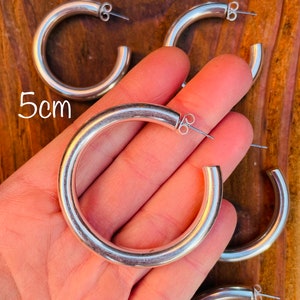 May include: Silver hoop earrings with a 5cm diameter. The earrings are thick and have a smooth, polished finish.