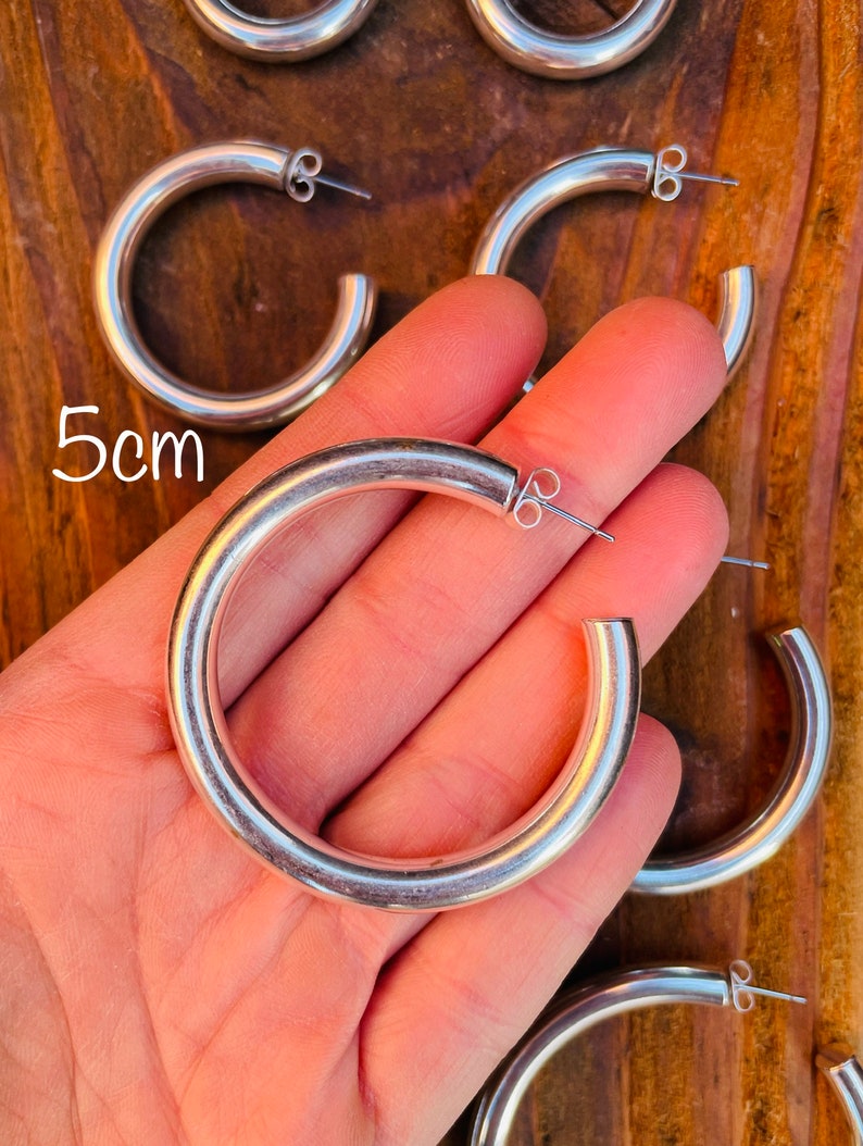 May include: Silver hoop earrings with a 5cm diameter. The earrings are thick and have a smooth, polished finish.