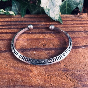 Peut inclure: Un bracelet en argent avec un motif géométrique. Le bracelet a un design simple avec un motif répétitif de triangles et de lignes.
