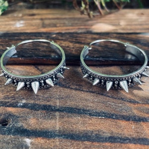May include: A pair of silver hoop earrings with a row of pointed spikes around the edge.