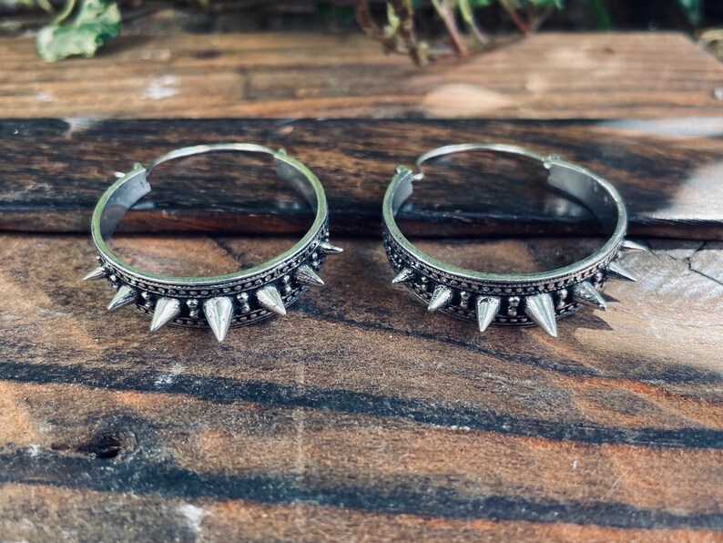 May include: A pair of silver hoop earrings with a row of pointed spikes around the edge.
