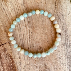 May include: A light blue and white beaded bracelet made of natural stones. The bracelet is made of round beads and is strung on a clear elastic cord.