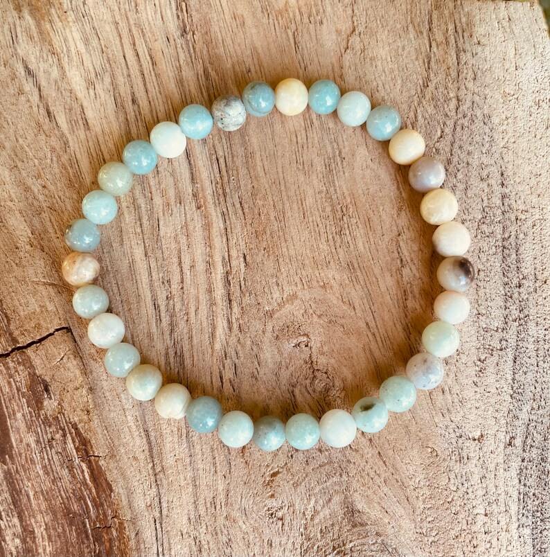 May include: A light blue and white beaded bracelet made of natural stones. The bracelet is made of round beads and is strung on a clear elastic cord.