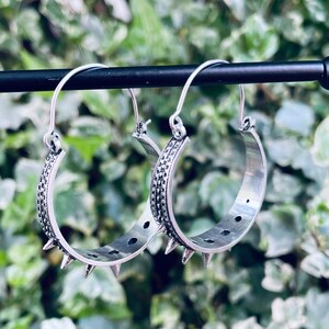 May include: A pair of silver hoop earrings with a textured design and spikes around the edge.