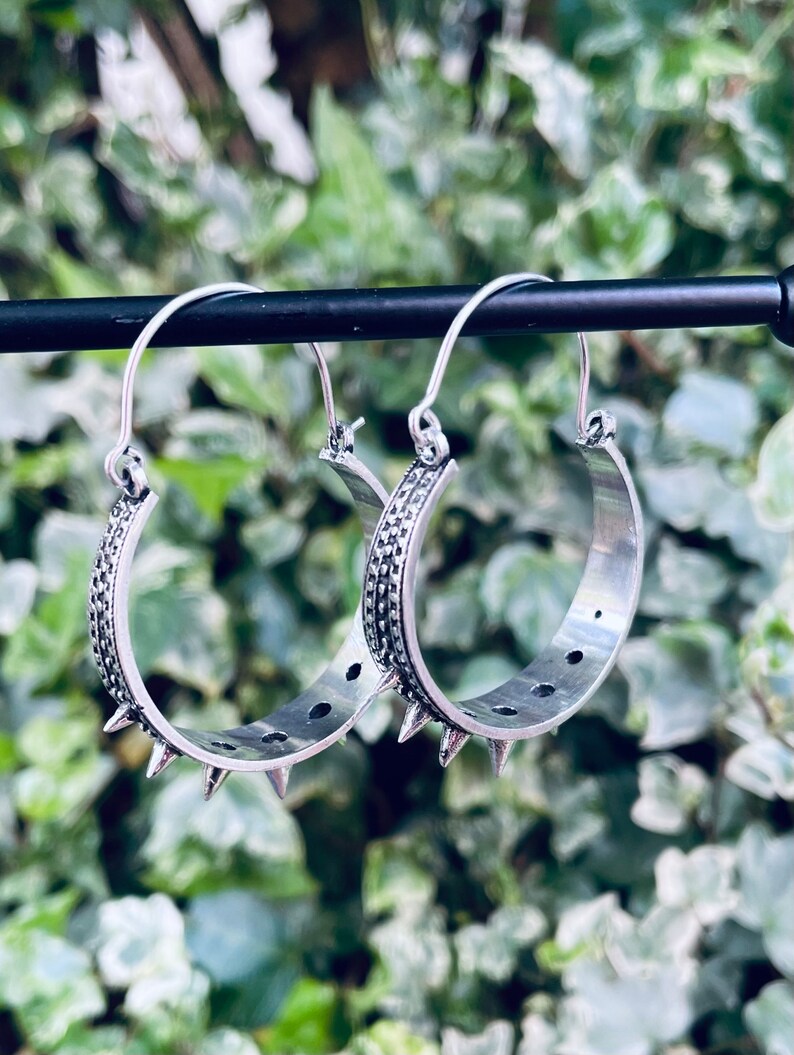 May include: A pair of silver hoop earrings with a textured design and spikes around the edge.