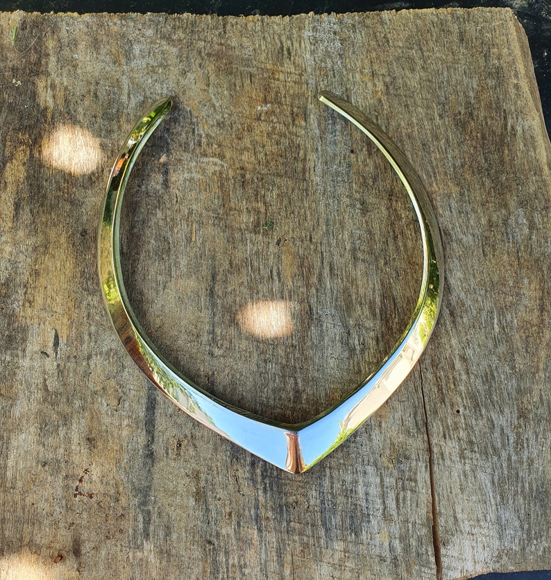 May include: A silver metal necklace with a V-shaped design. The necklace is lying on a wooden surface.
