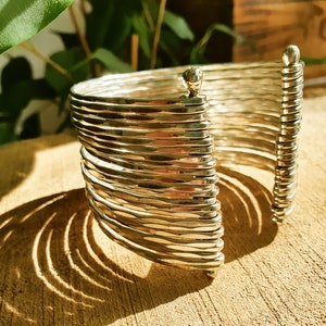 May include: A silver bracelet with a hammered finish and a unique design. The bracelet is made of multiple thin bands that are stacked on top of each other.
