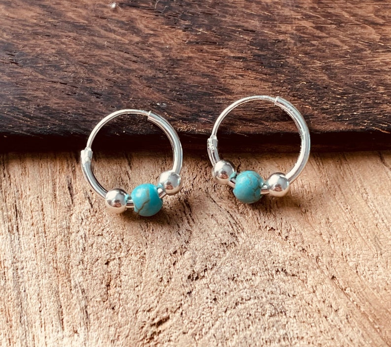 May include: A pair of silver hoop earrings with turquoise beads. The earrings are small and delicate.