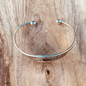 May include: A silver bangle bracelet with a geometric design. The bracelet has rounded ends.