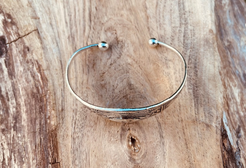 May include: A silver bangle bracelet with a geometric design. The bracelet has rounded ends.