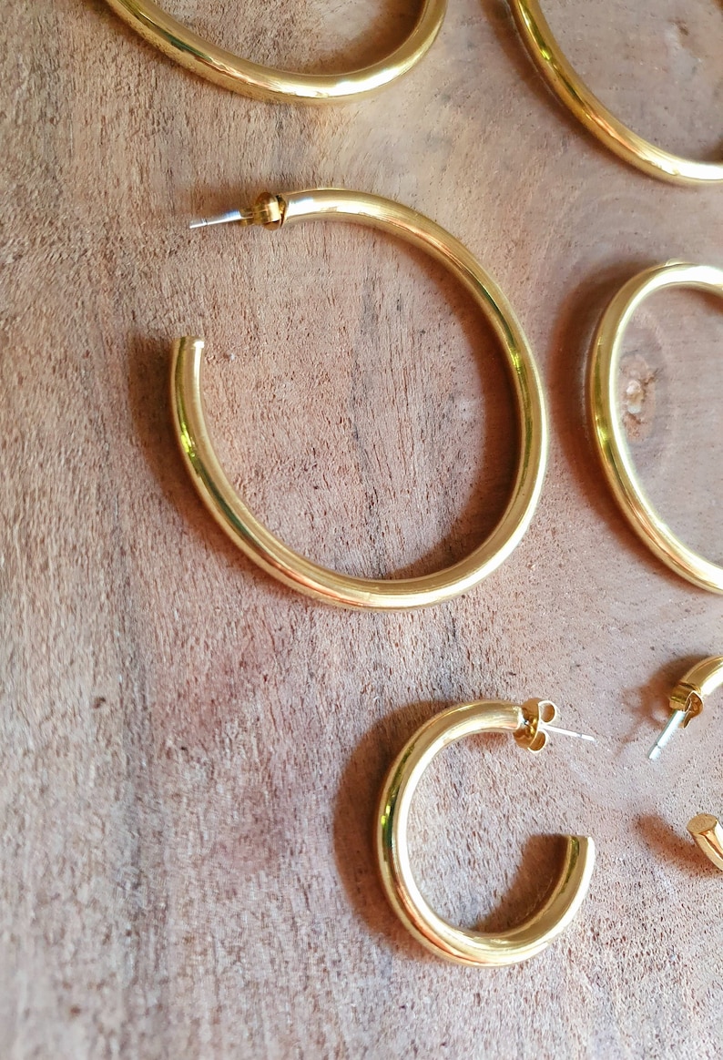 May include: Set of four gold hoop earrings of varying sizes. The earrings are made of a thick, round metal and have a polished finish.