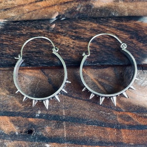 May include: A pair of silver hoop earrings with spikes around the edge.