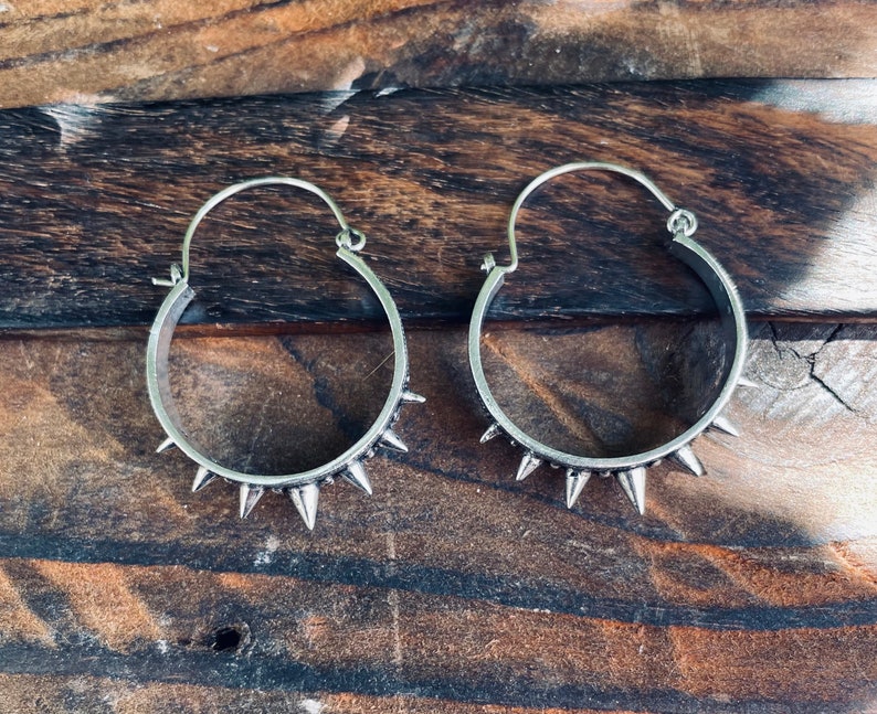 May include: A pair of silver hoop earrings with spikes around the edge.