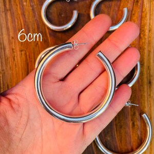 May include: Silver hoop earrings with a 6 cm diameter. The earrings are thick and have a smooth finish.