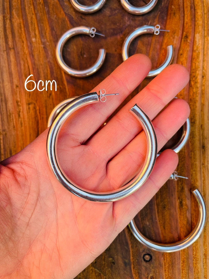 May include: Silver hoop earrings with a 6 cm diameter. The earrings are thick and have a smooth finish.