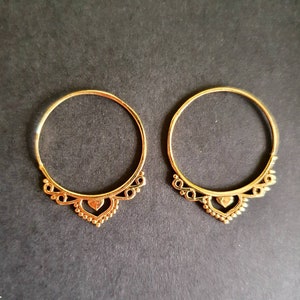 Può includere: Due orecchini a cerchio dorati con un design a forma di cuore nella parte inferiore.