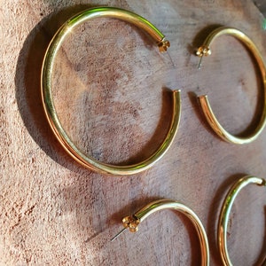 May include: Three pairs of gold hoop earrings of different sizes. The earrings are on a wooden surface.
