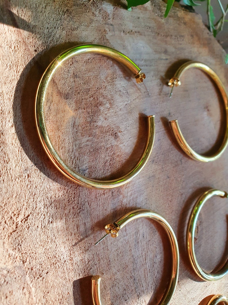 May include: Three pairs of gold hoop earrings of different sizes. The earrings are on a wooden surface.